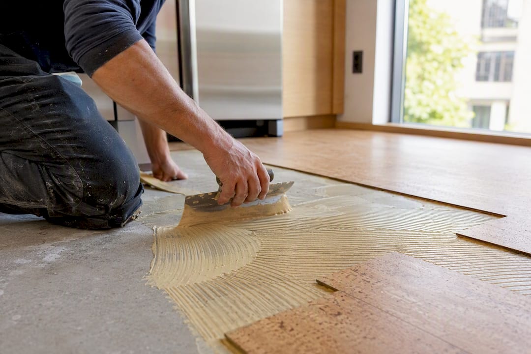 Hands applying adhesive under cork flooring